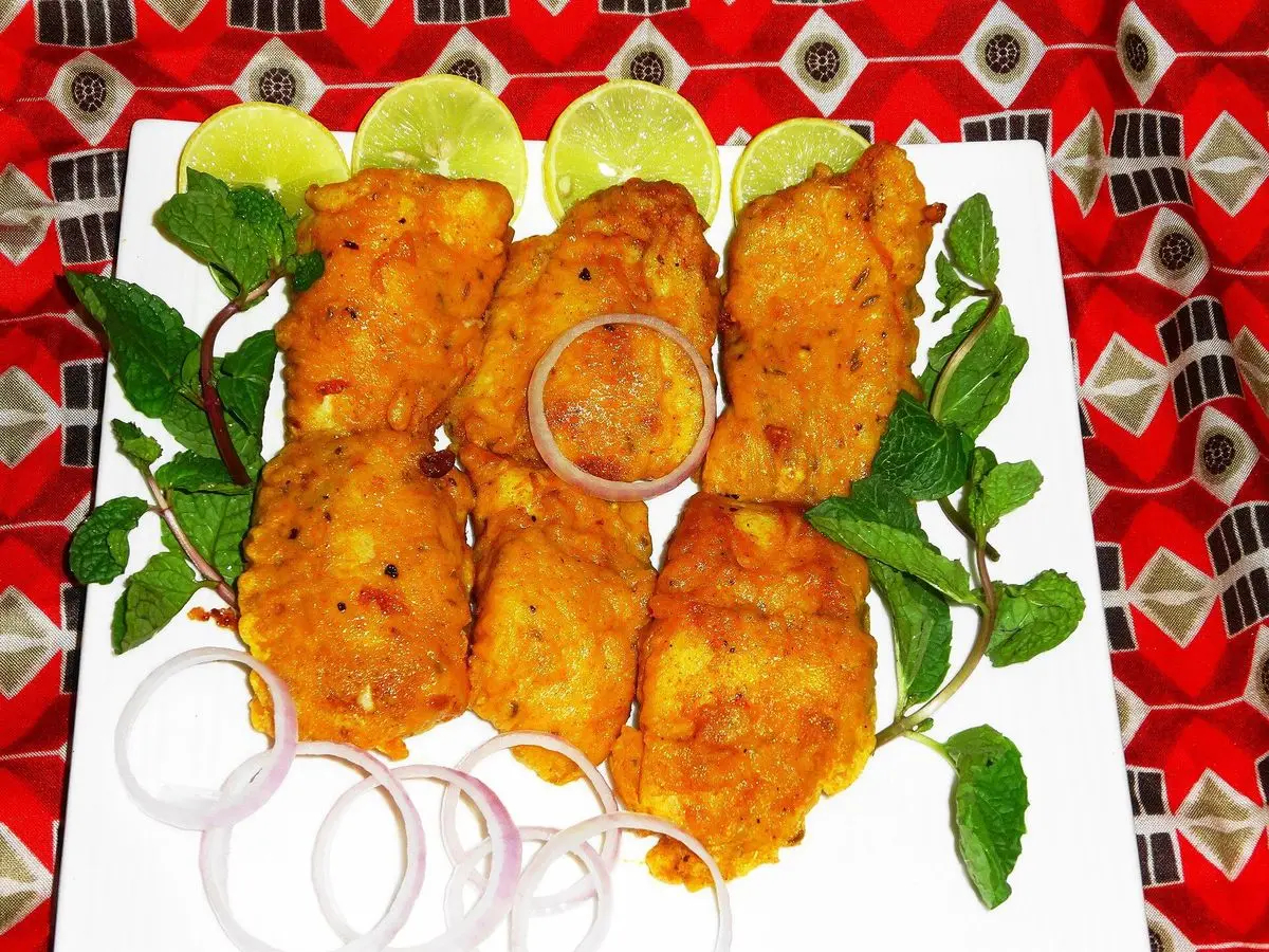 Trozos de pescado frito especiado con aros de cebolla, rodajas de lima y hojas de menta sobre una fuente blanca