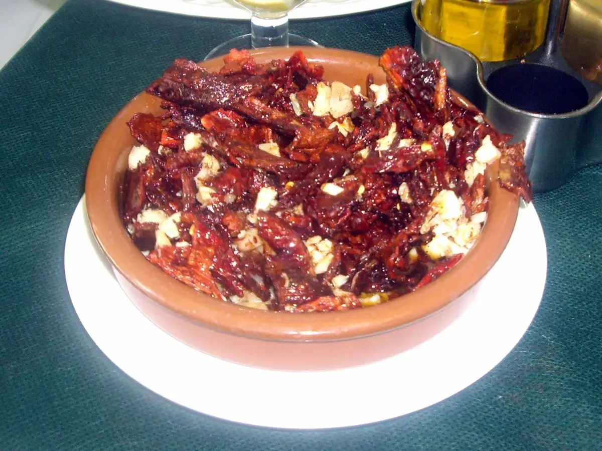 Cazuela de barro con pimientos secos fritos, trozos de bacalao y ajo en aceite de oliva