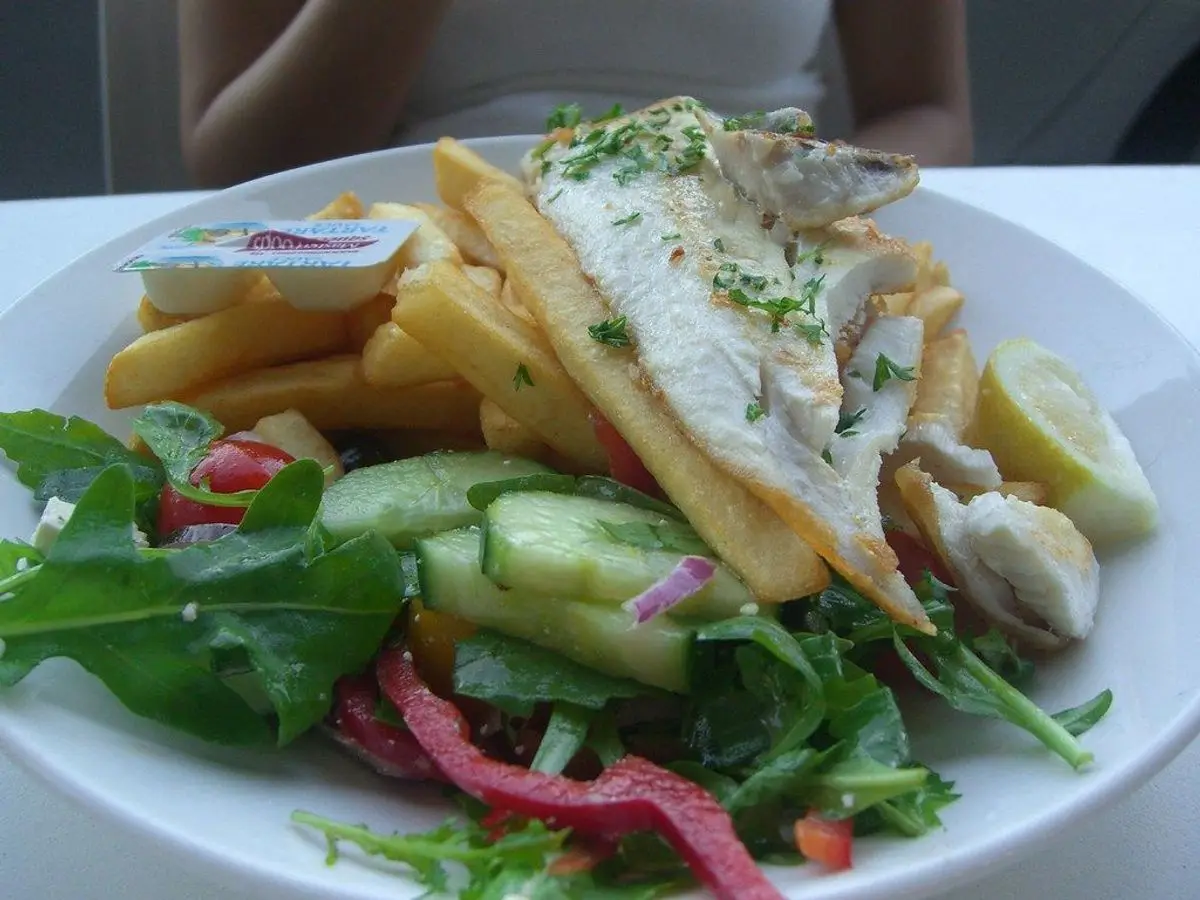 Filete de pescado blanco con patatas fritas, ensalada de hojas y tomate en un plato