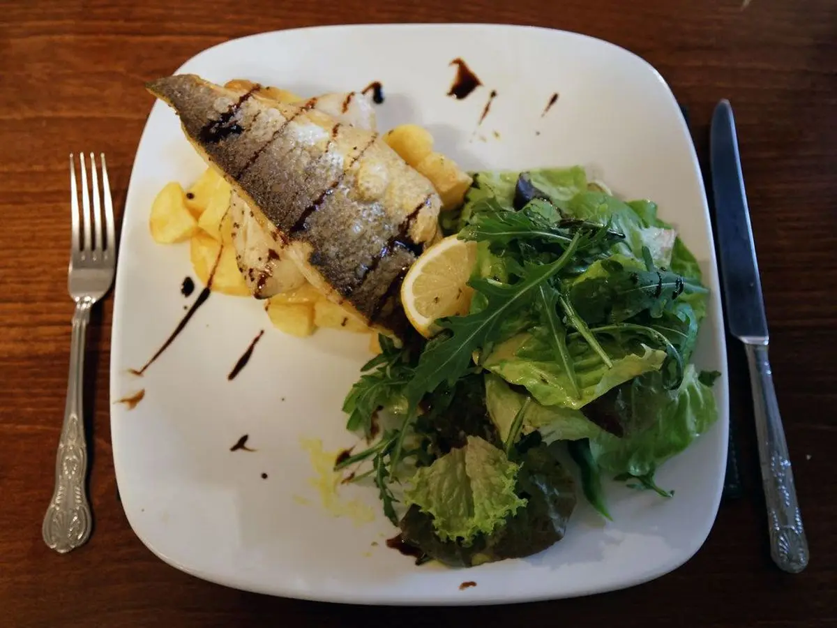 Filete de pescado a la plancha con limón sobre ensalada de rúcula en un plato cuadrado