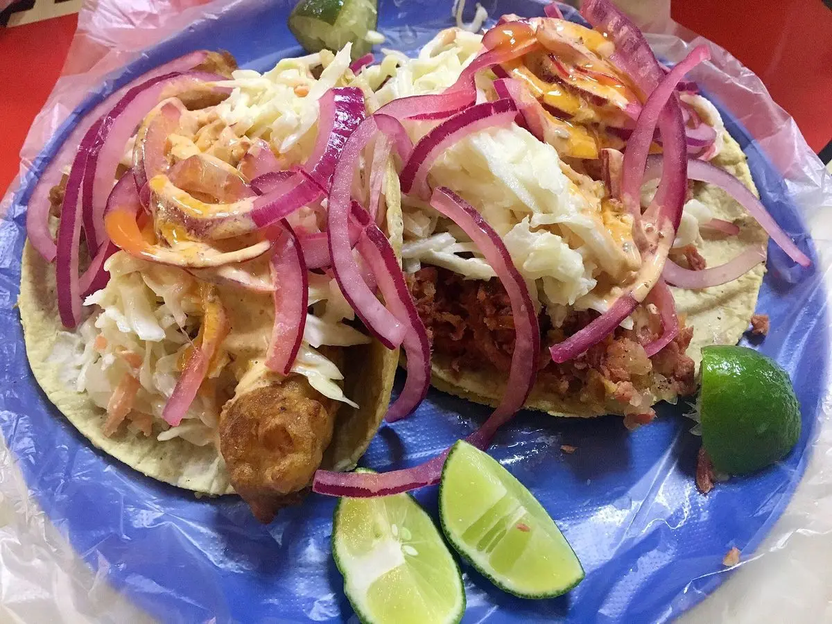 Tacos de pescado en tortilla con cebolla morada encurtida, repollo y lima en plato azul