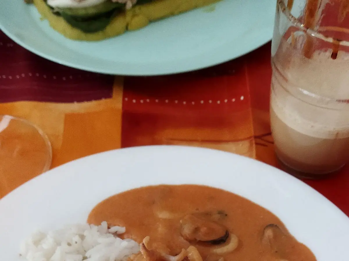 Pescado cubierto de salsa anaranjada de mariscos con calamares y mejillones junto a arroz blanco