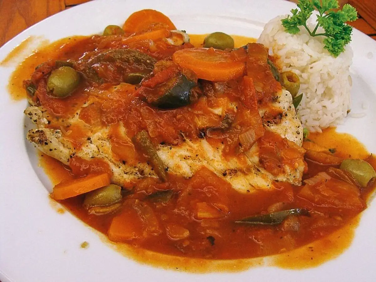 Filete de pescado en salsa de tomate con aceitunas y zanahoria, junto a arroz blanco