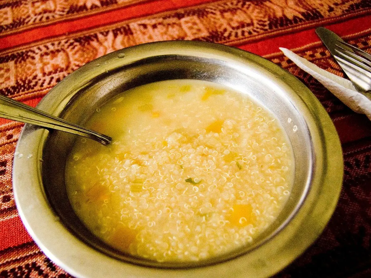 Cuenco metálico de sopa espesa de quinoa amarillenta con cuchara sobre un mantel andino
