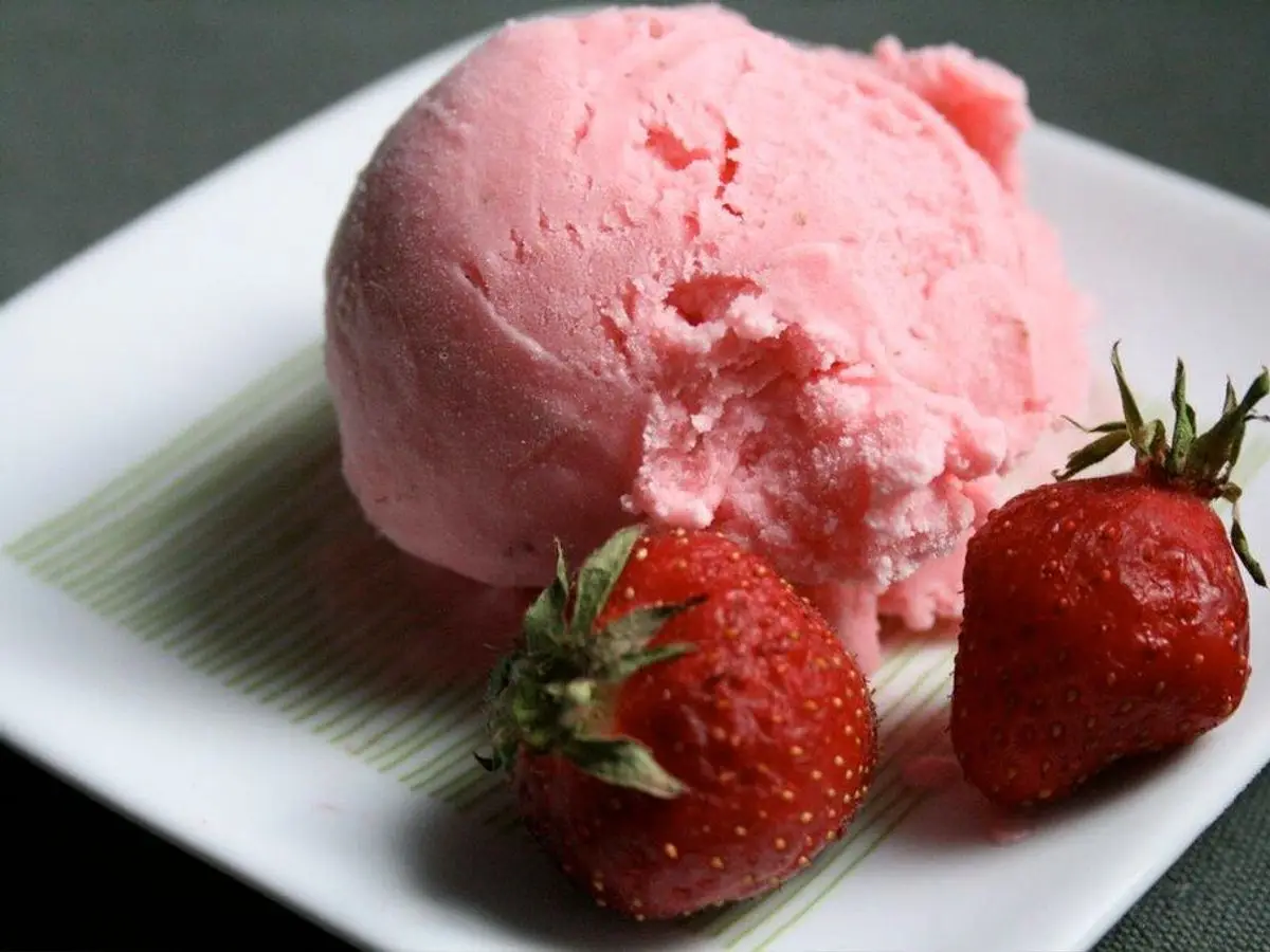 Bola de helado o yogur helado rosa de fresa en un plato blanco con dos fresas frescas