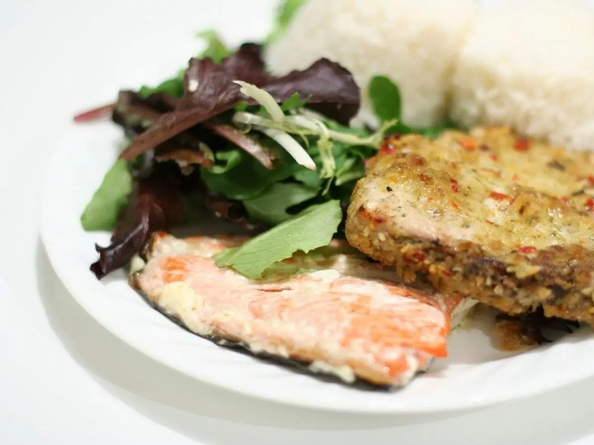 Filete de pescado a la plancha con arroz blanco y ensalada de hojas verdes en plato blanco