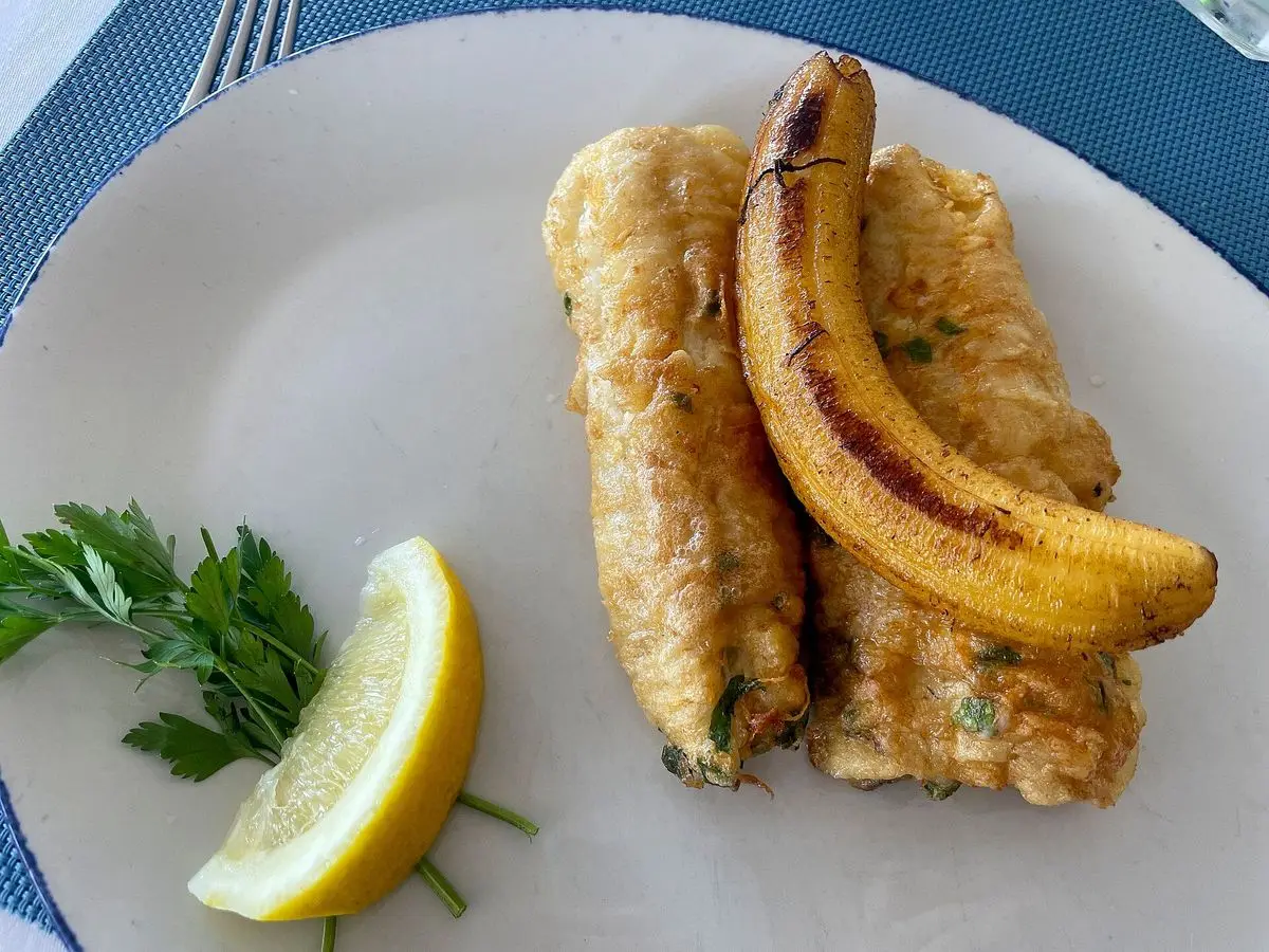 Filetes de pescado empanado con plátano frito, limón y perejil en un plato