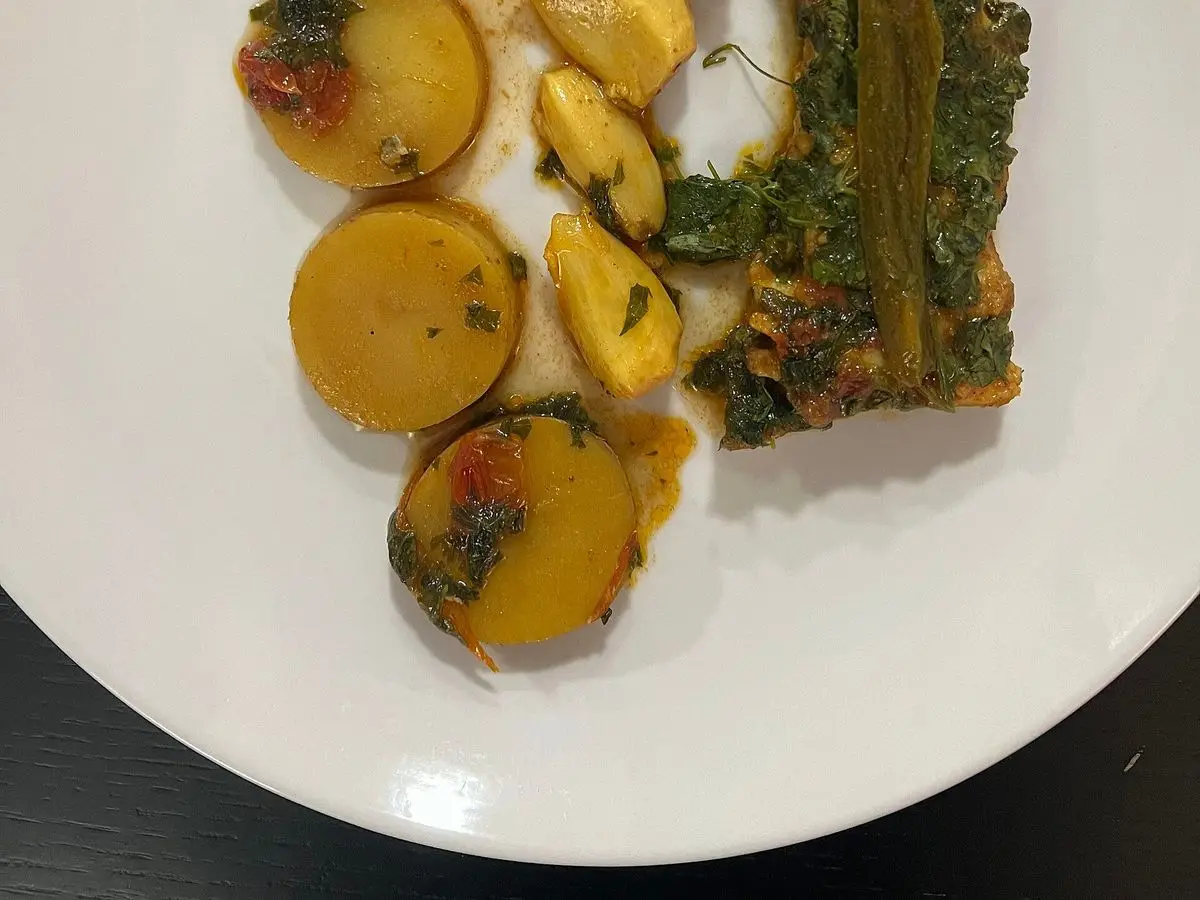 Filete de pescado con rodajas de patata y hierbas picadas en salsa verde sobre un plato blanco