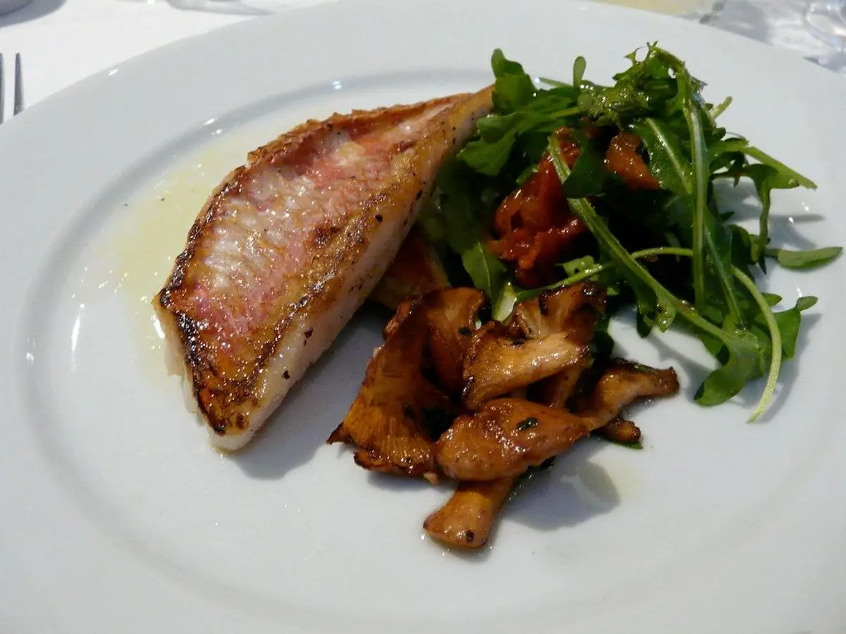 Filete de pescado a la plancha con setas salteadas y rúcula en un plato blanco