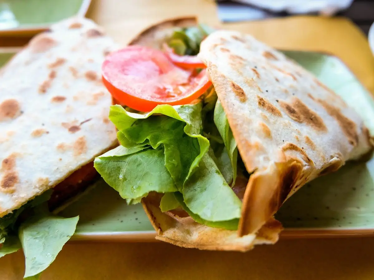 Piadina doblada rellena de hojas verdes y rodajas de tomate sobre un plato verde