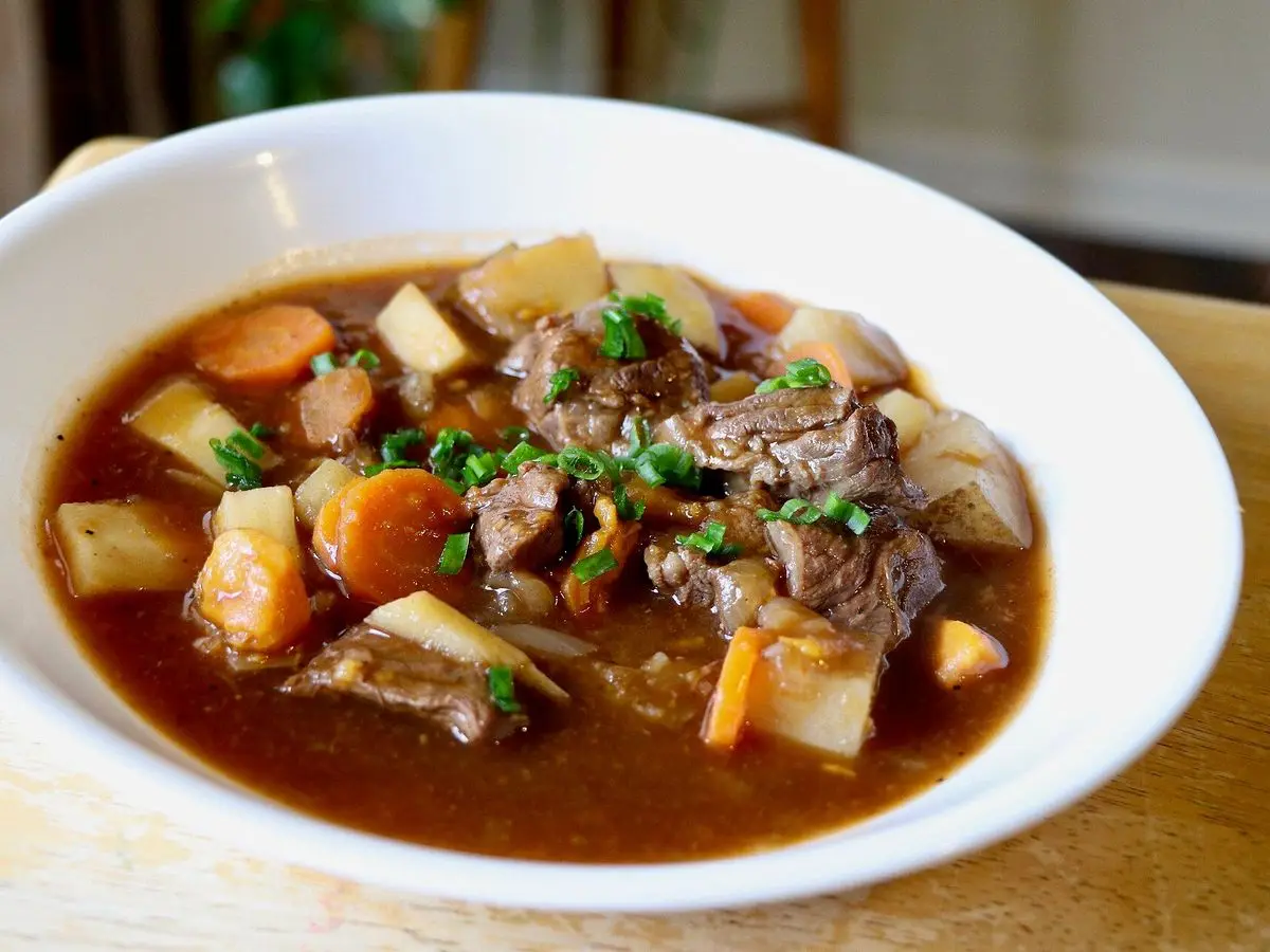 Plato hondo de guiso de ternera con patata, zanahoria y perejil sobre un mantel de madera