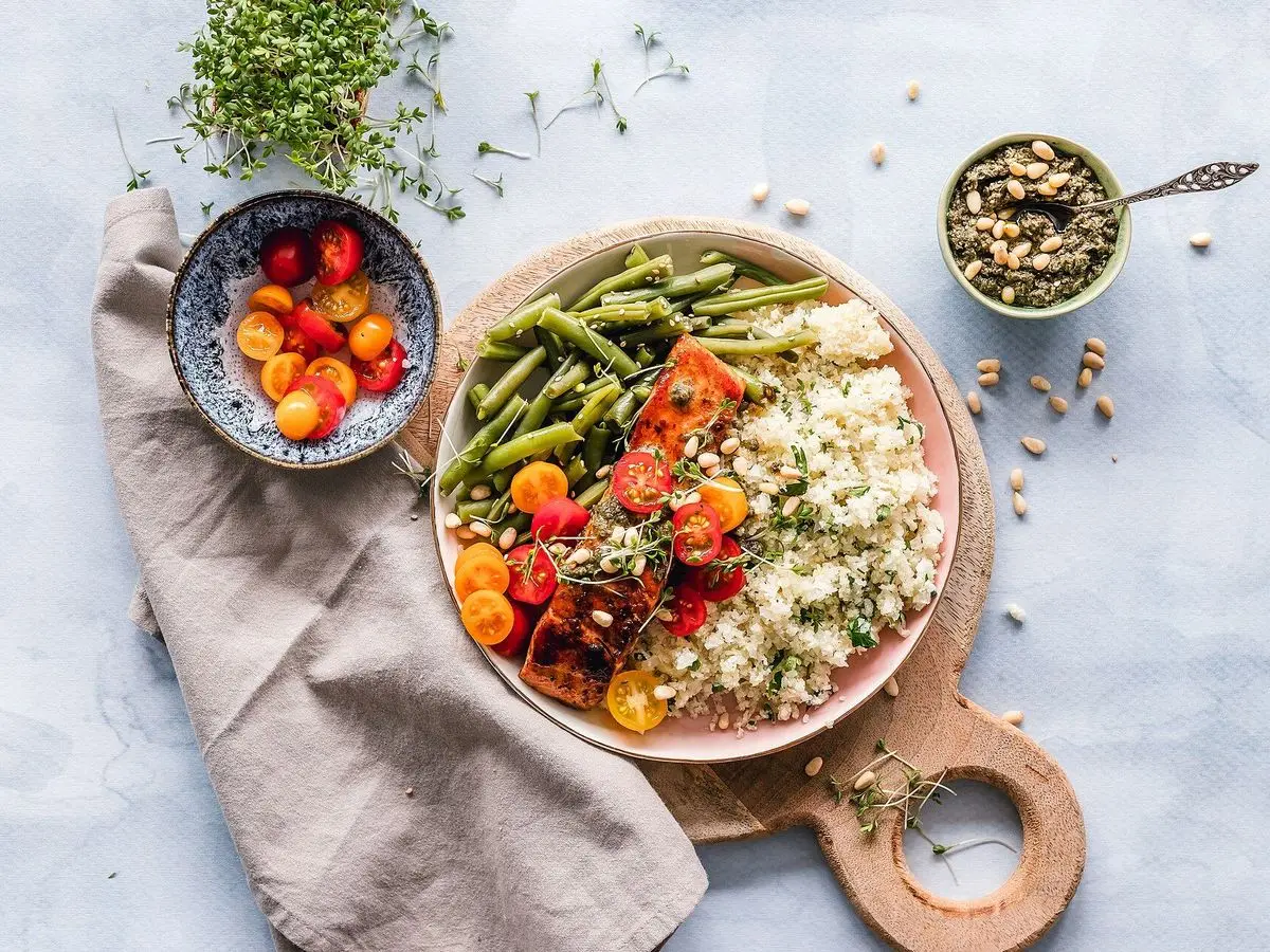 Plato de madera con quinoa, judías verdes y tomates cherry junto a especias sobre mesa clara
