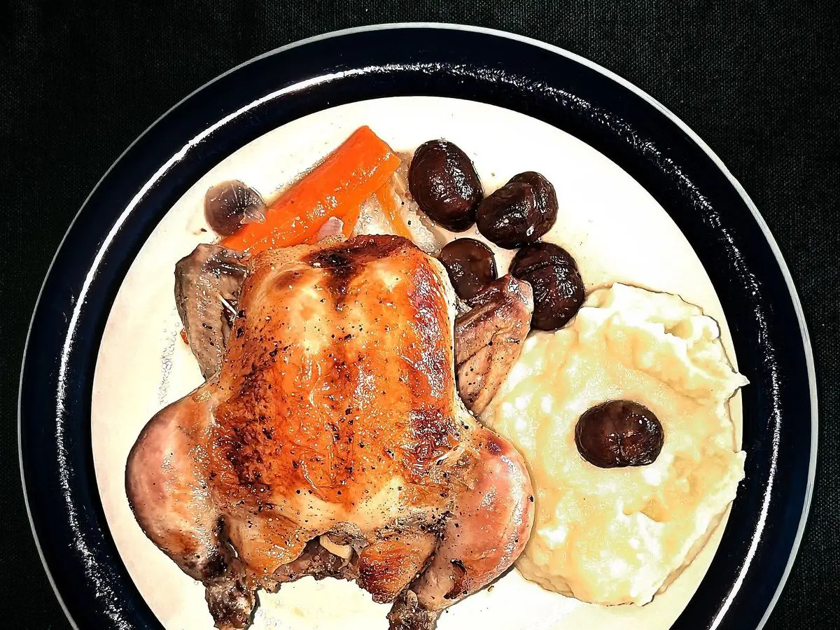 Ave pequeña asada dorada en un plato con zanahoria, castañas y puré