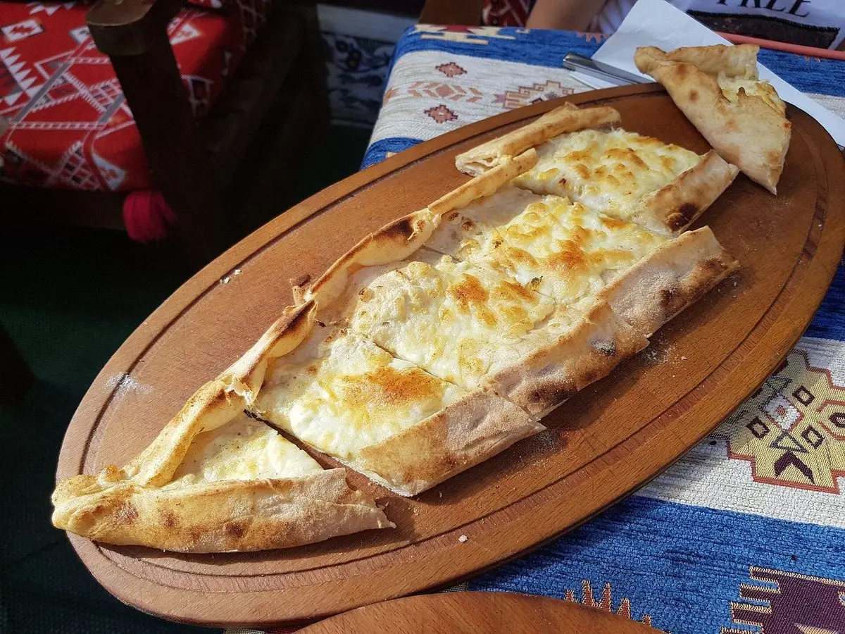 Pide turco alargado gratinado con queso sobre una bandeja de madera