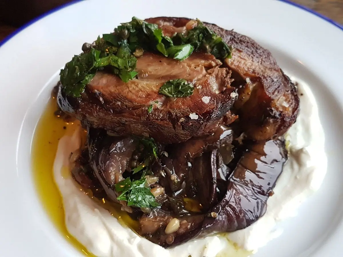 Cordero asado con hierbas sobre un puré blanco cremoso en un plato blanco