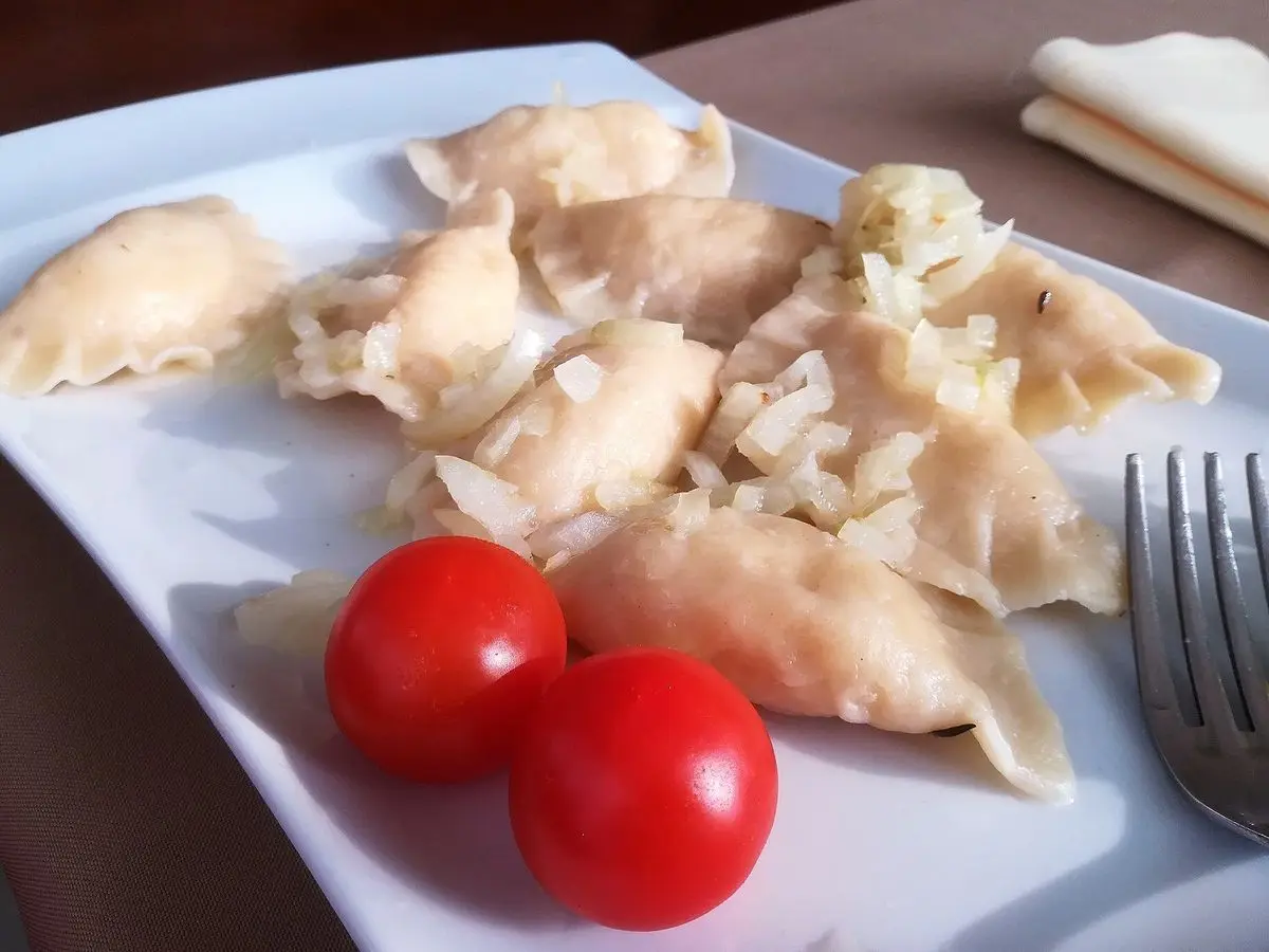 Pierogi con cebolla dorada y tomates cherry en un plato blanco cuadrado