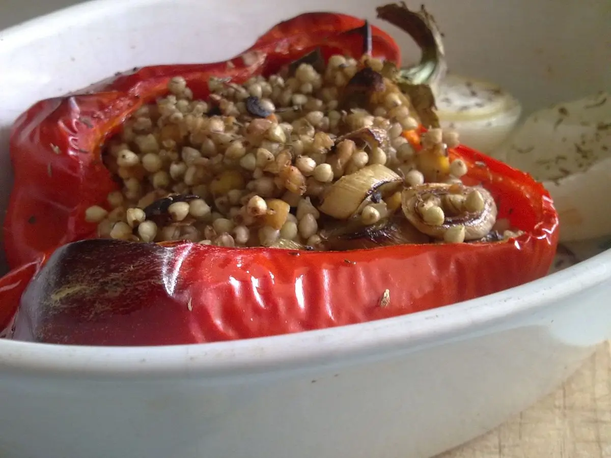 Pimiento rojo asado relleno de grano cocido en una fuente blanca