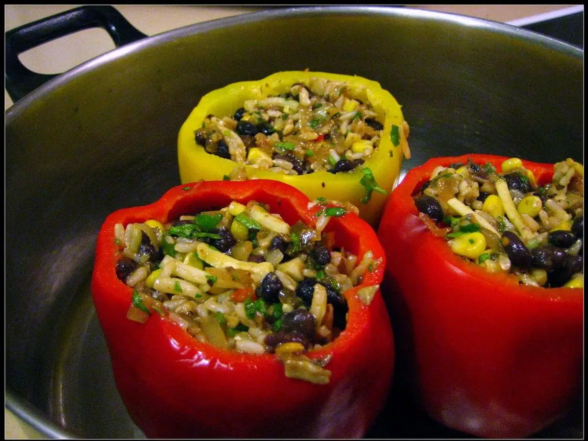 Pimientos rojos y uno amarillo rellenos de arroz y verduras, servidos en una cazuela metálica