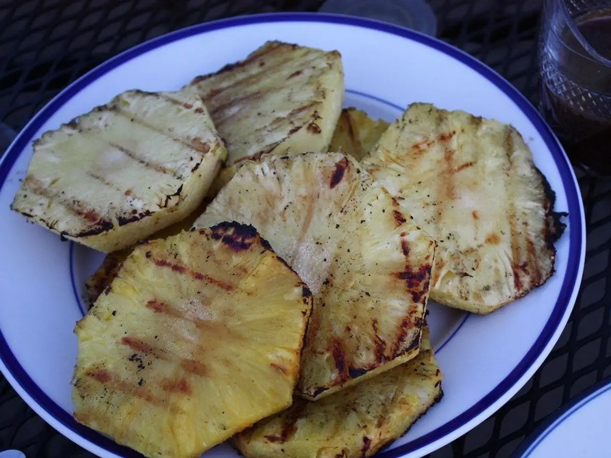 Rodajas de piña a la plancha con marcas de parrilla servidas en un plato blanco con borde azul