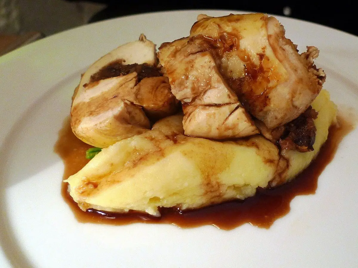 Pintada asada en trozos sobre puré de patata con salsa oscura en un plato blanco