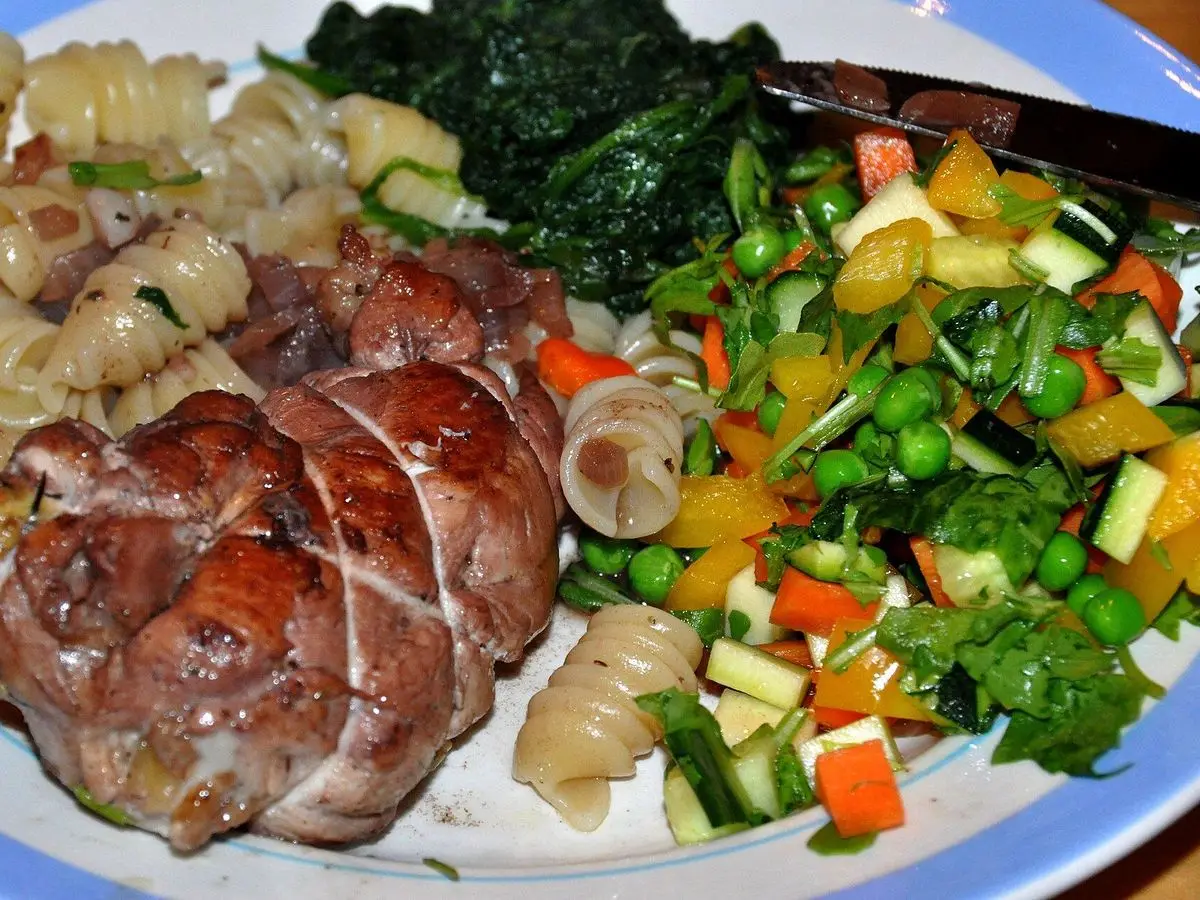 Pintada rellena asada en rodajas con verduras salteadas y pasta en un plato