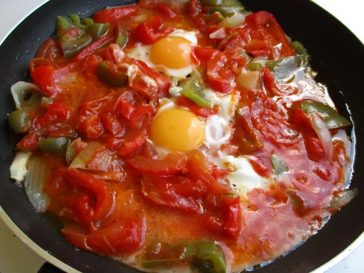 Sartén negra con pimientos y tomate guisados con huevos escalfados