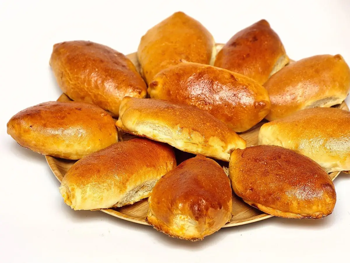 Pirozhki rusos al horno, panecillos dorados y brillantes rellenos, apilados en una fuente