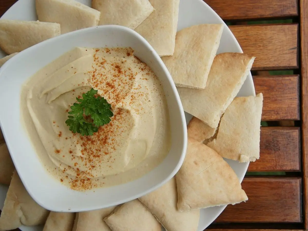 Cuenco blanco de hummus con pimentón y perejil rodeado de triángulos de pan de pita