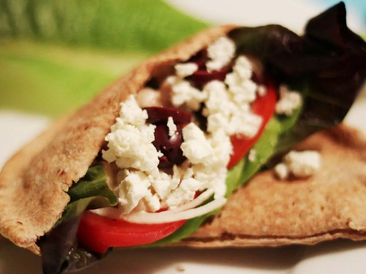 Pan de pita integral relleno de lechuga, tomate, cebolla, queso feta desmenuzado y aceitunas negras