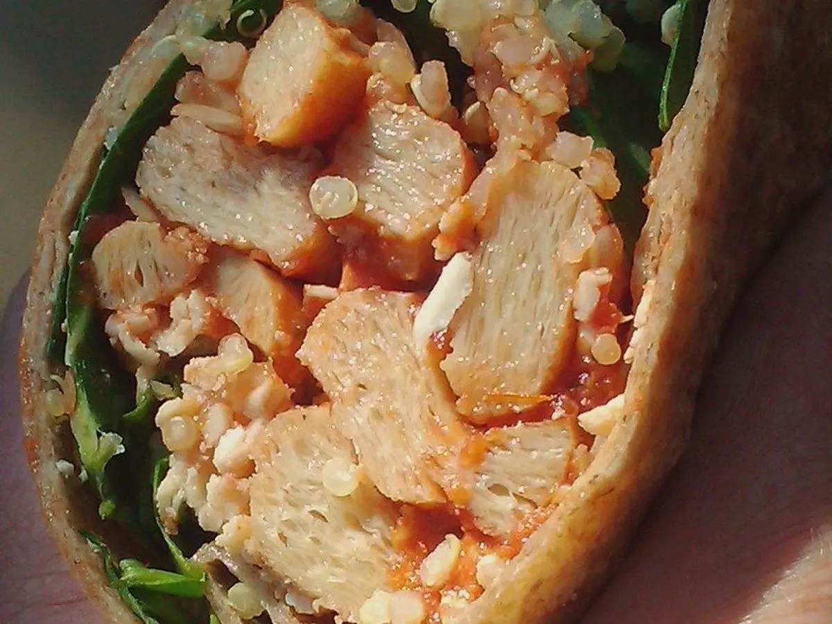 Pan relleno de trozos de seitán rebozado con salsa roja y hojas verdes en primer plano