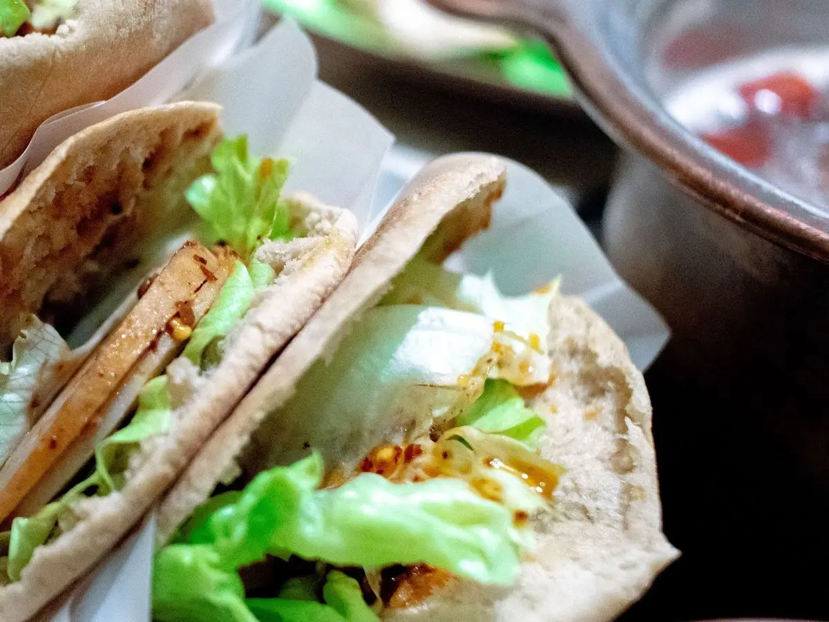 Panes de pita rellenos de lechuga y lonchas de tofu dorado con salsa especiada, envueltos en papel