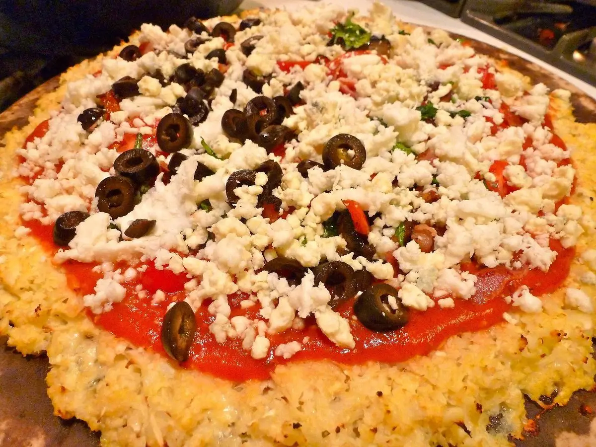 Pizza de base de coliflor con salsa de tomate, queso desmenuzado y aceitunas