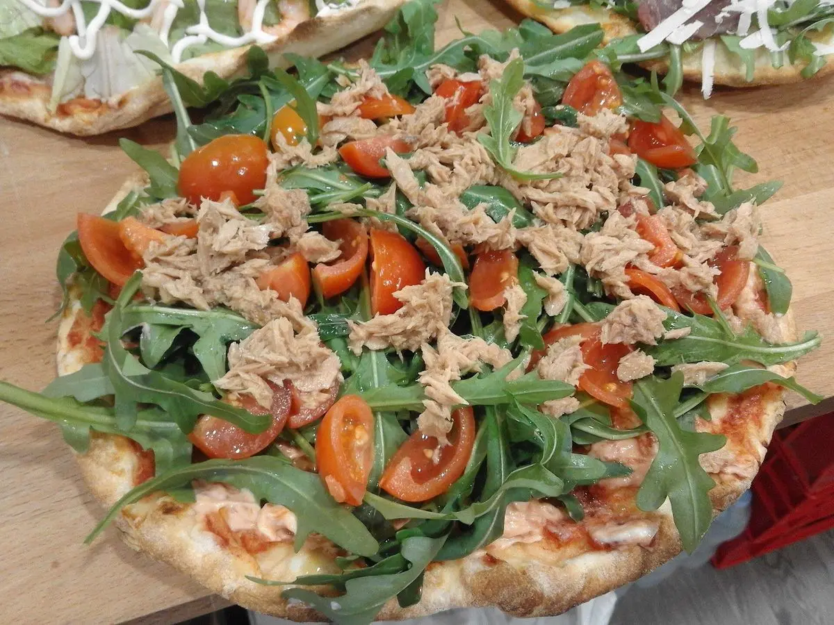 Pizza con atún, rúcula y tomate cherry sobre una tabla de madera