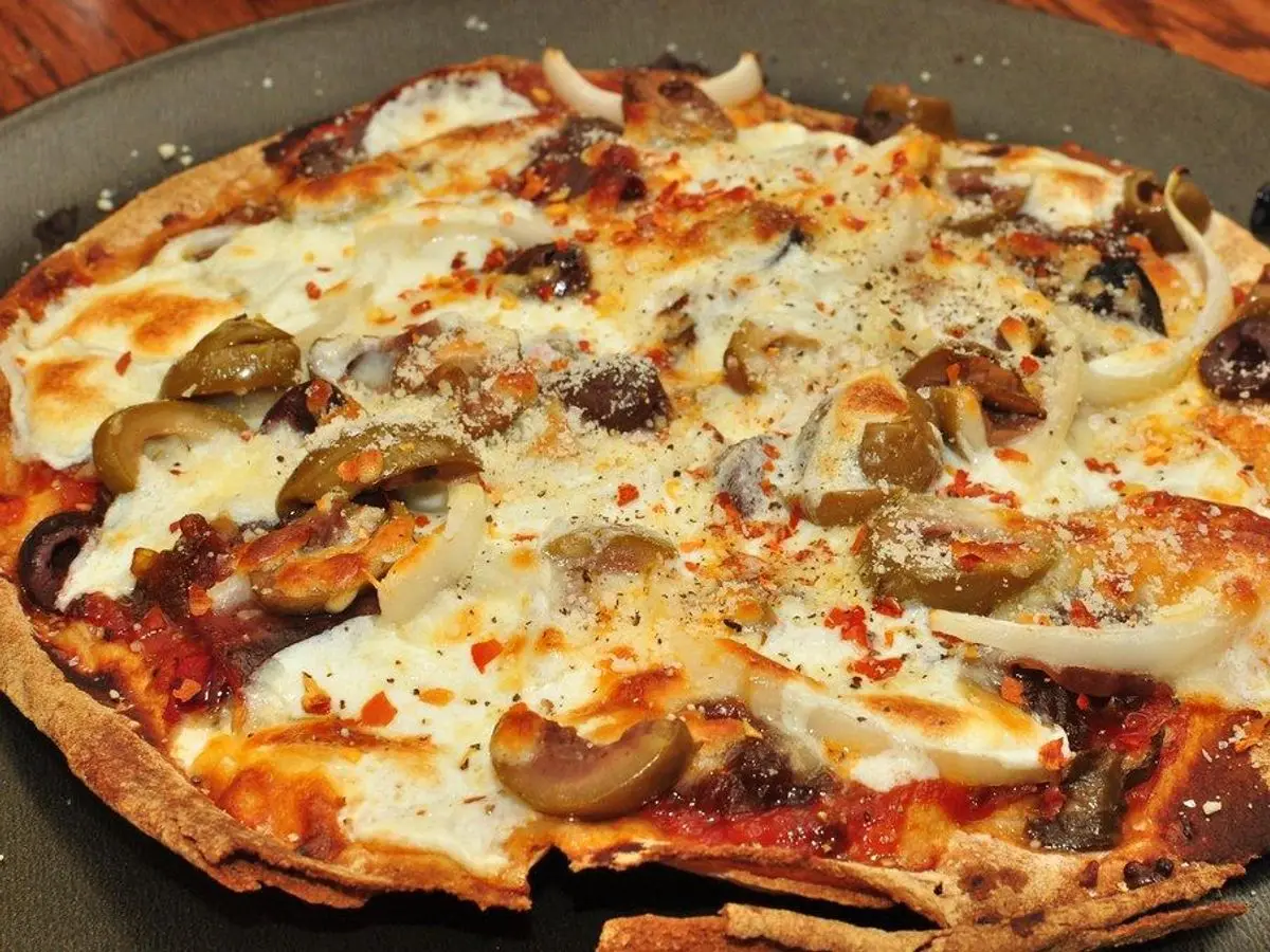 Pizza casera con queso mozzarella fundido, champiñones, aceitunas y cebolla sobre una bandeja