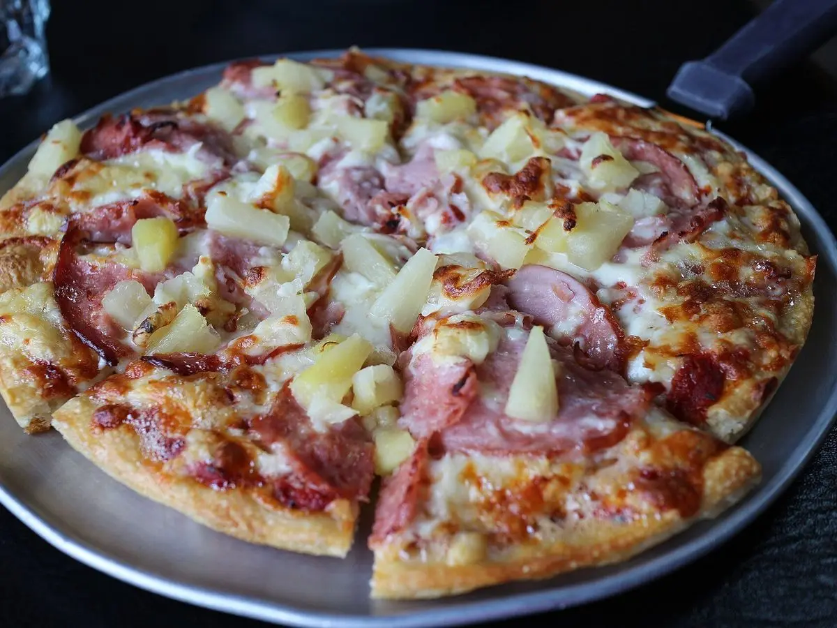 Pizza hawaiana con jamón y trozos de piña sobre una bandeja metálica