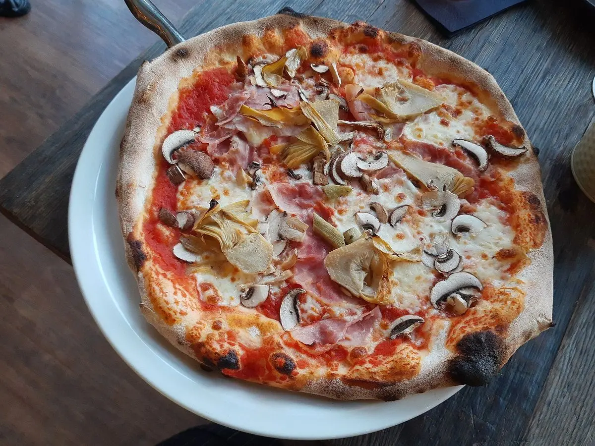 Pizza con jamón cocido, champiñones laminados y tomate en un plato blanco