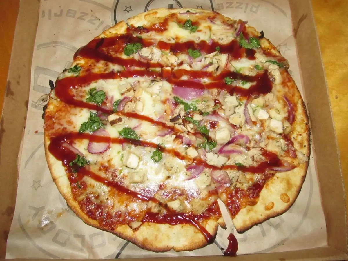 Pizza con pollo, cebolla morada y un hilo de salsa barbacoa sobre papel