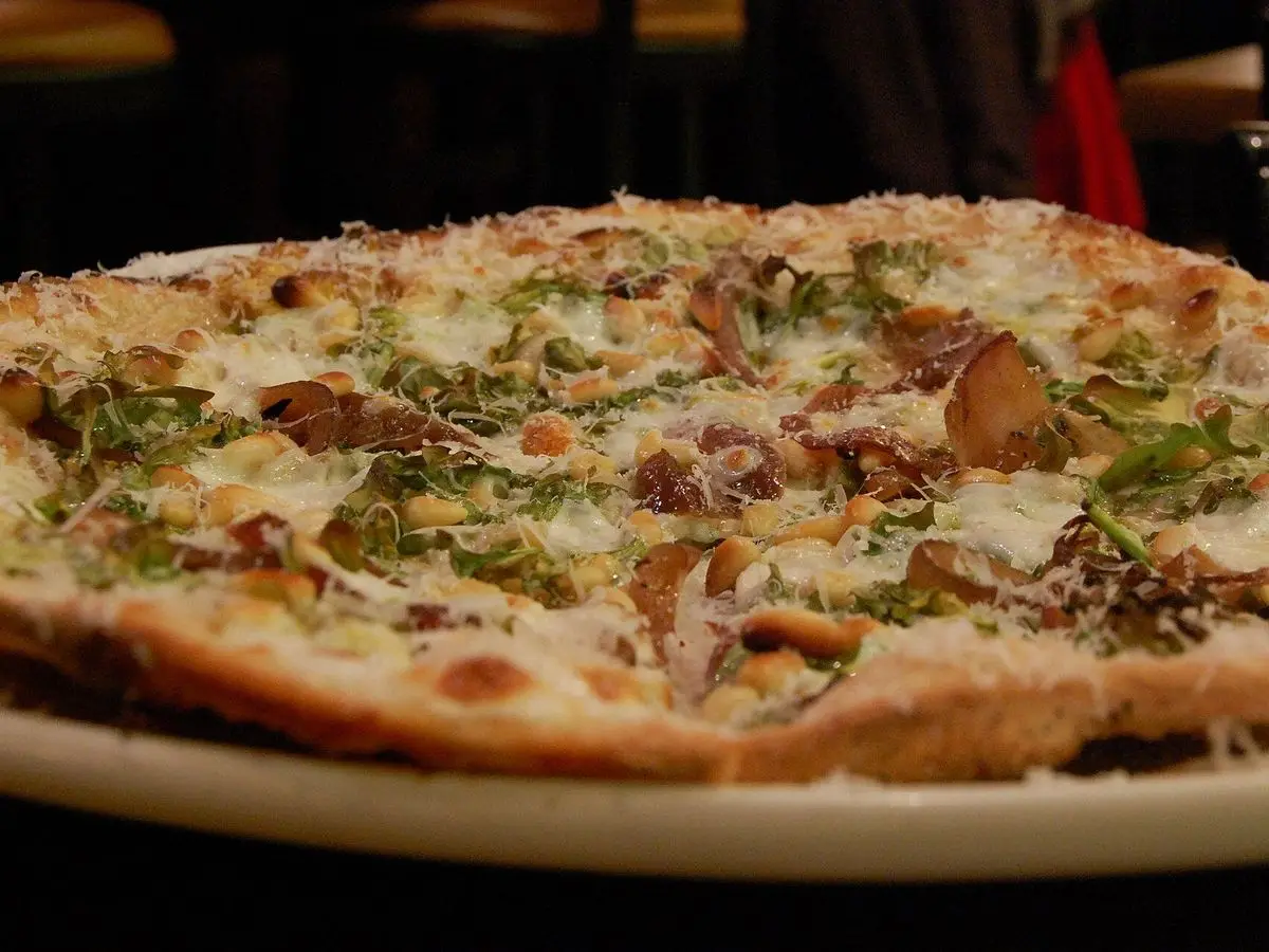 Pizza de masa fina con queso, rodajas de champiñón y rúcula por encima sobre un plato blanco
