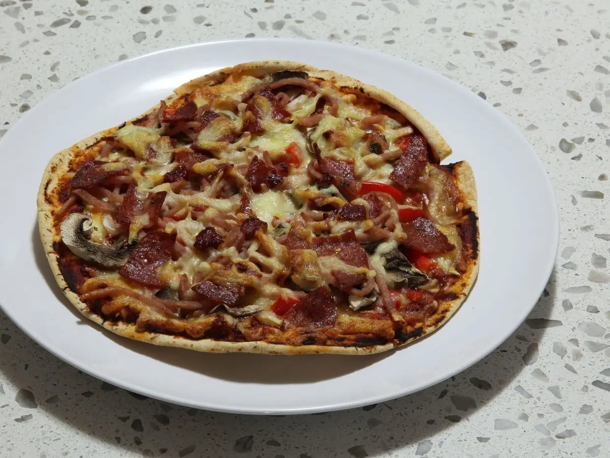 Pizza fina sobre base plana con tomate y queso en un plato blanco