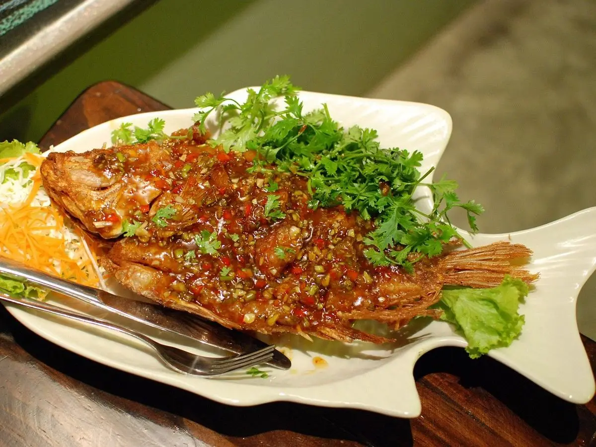 Pescado entero frito cubierto de salsa roja de guindilla y hierbas frescas sobre un plato blanco