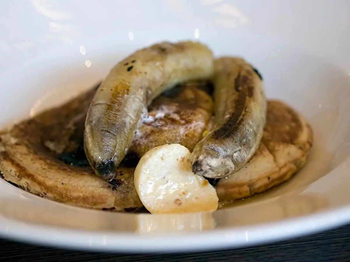 Plátanos asados y caramelizados en un plato hondo blanco, con su piel dorada