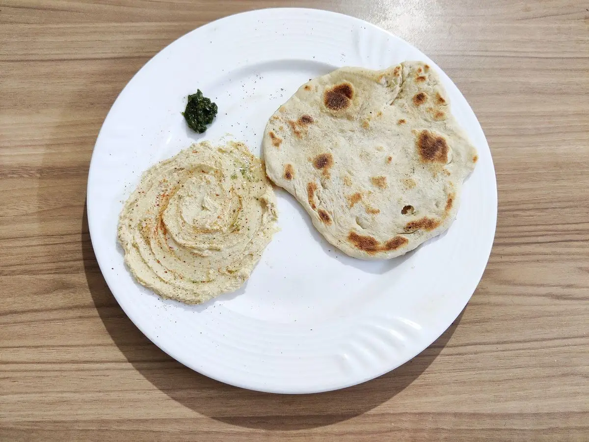 Plato blanco con hummus casero, pan de pita templado y un poco de especia por encima