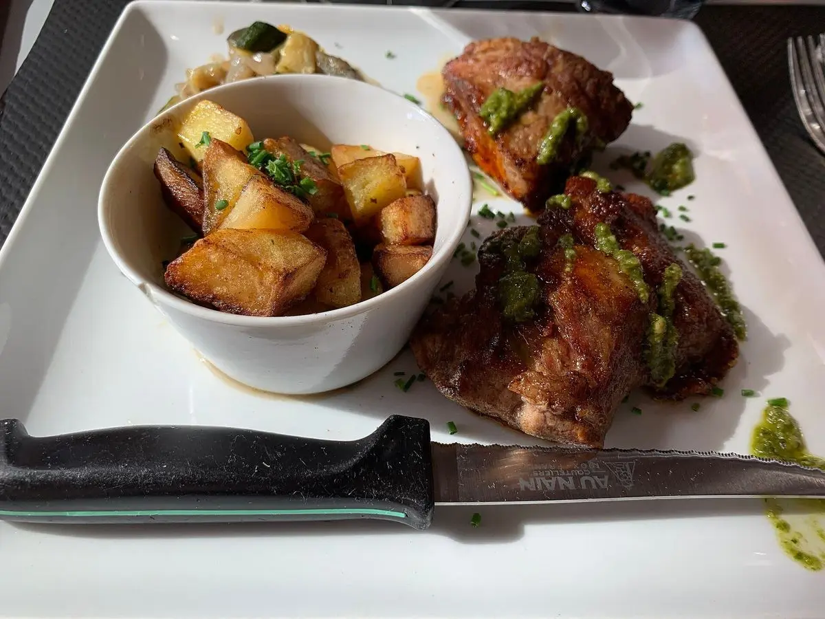 Pluma ibérica asada con patatas salteadas en un cuenco y salsa verde en un plato