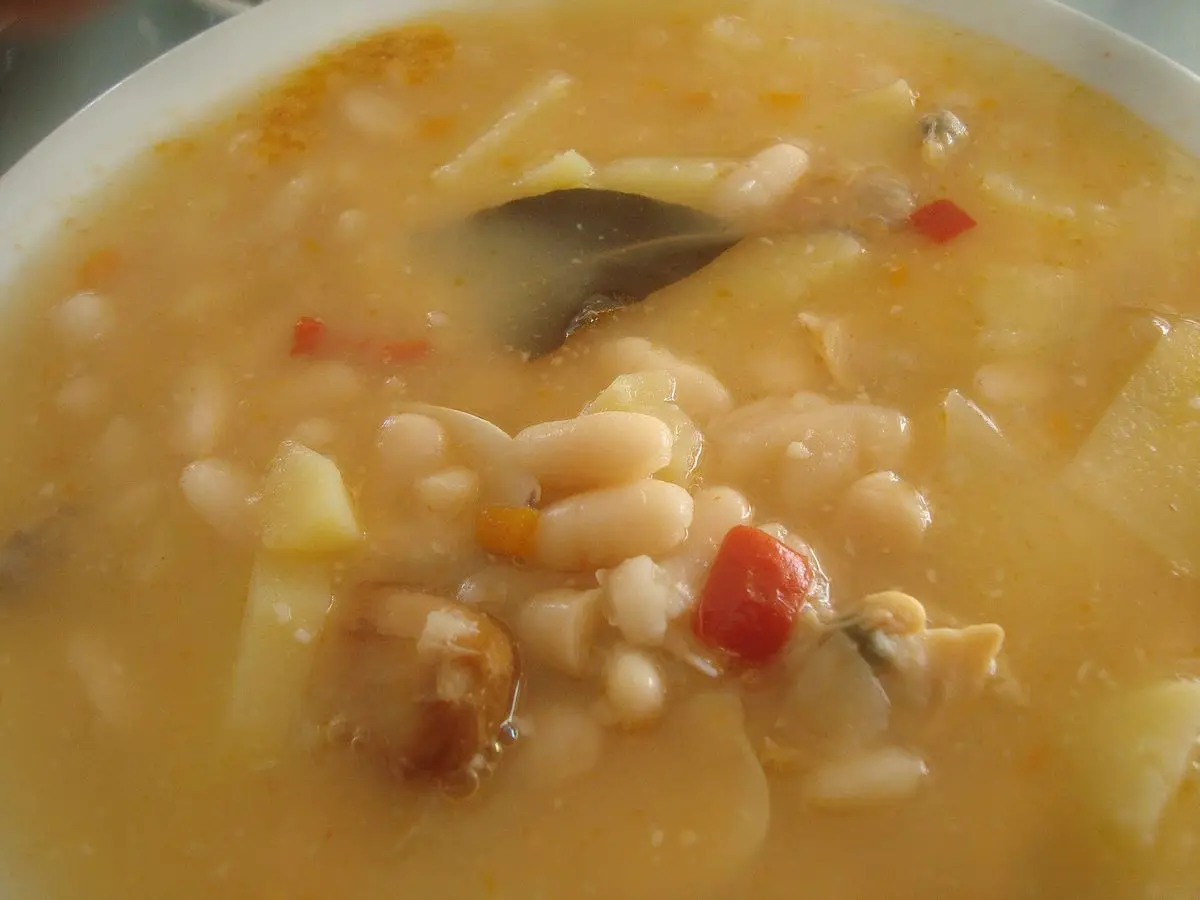 Cuenco de alubias blancas guisadas con almejas, patata y pimiento rojo