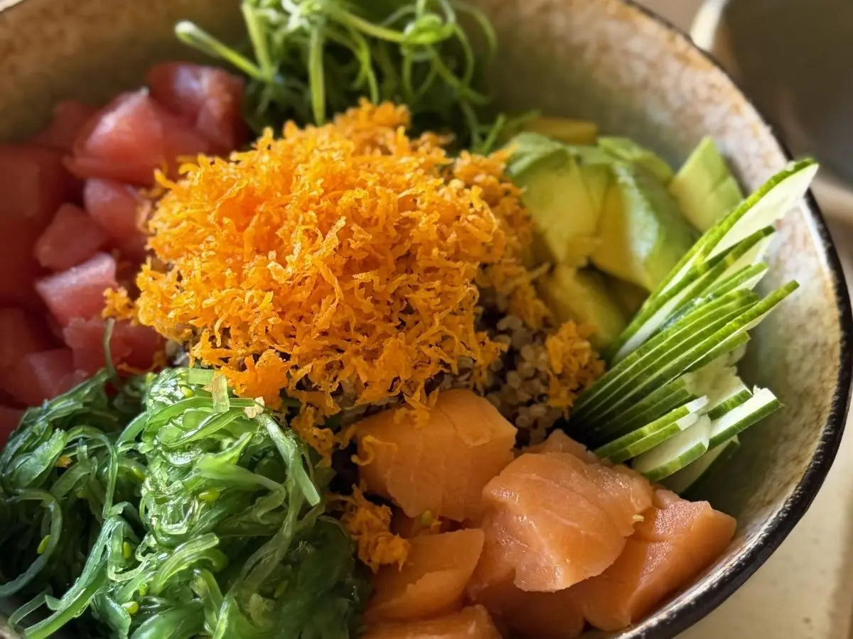 Bol poke con atún, salmón, aguacate, alga wakame y pepino en un cuenco de cerámica
