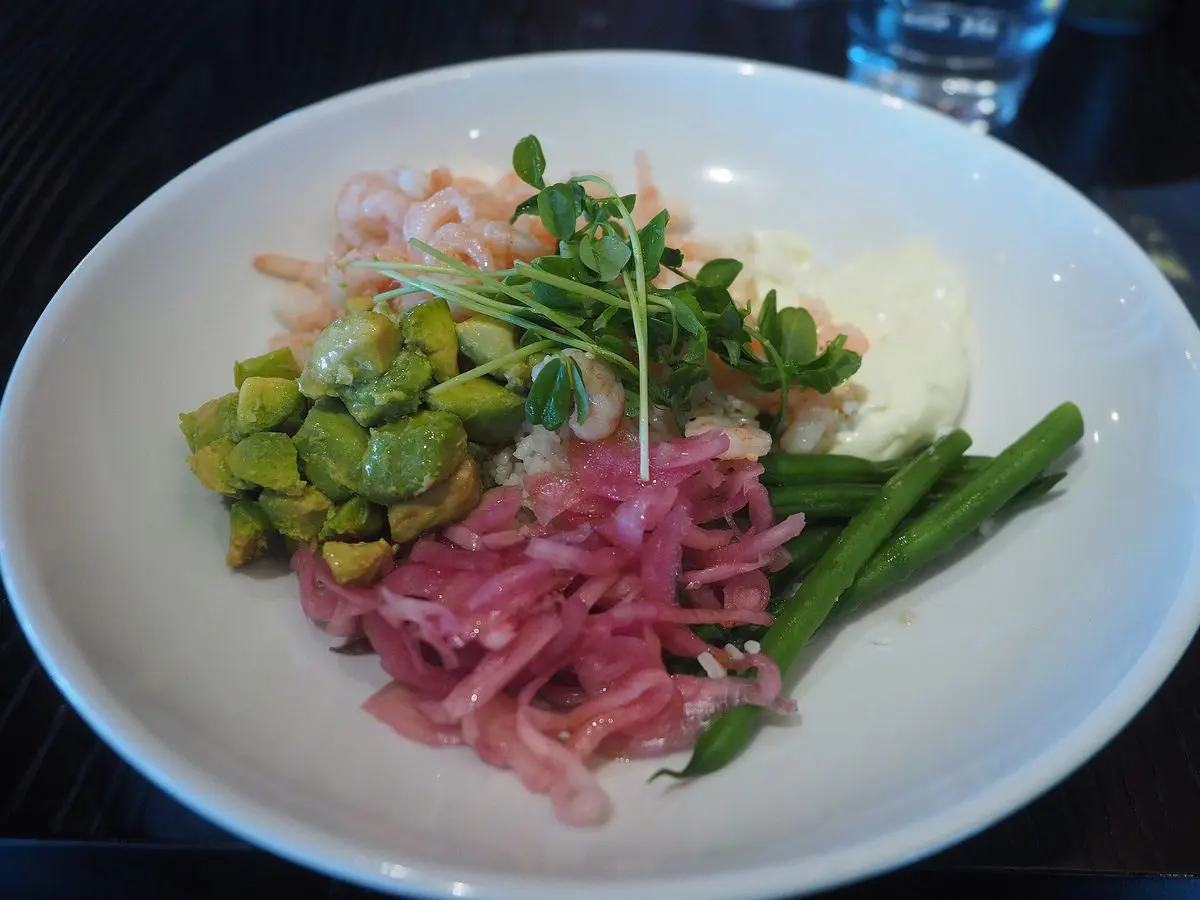 Plato hondo blanco con poke de gambas, edamame, cebolla encurtida rosa y judías verdes