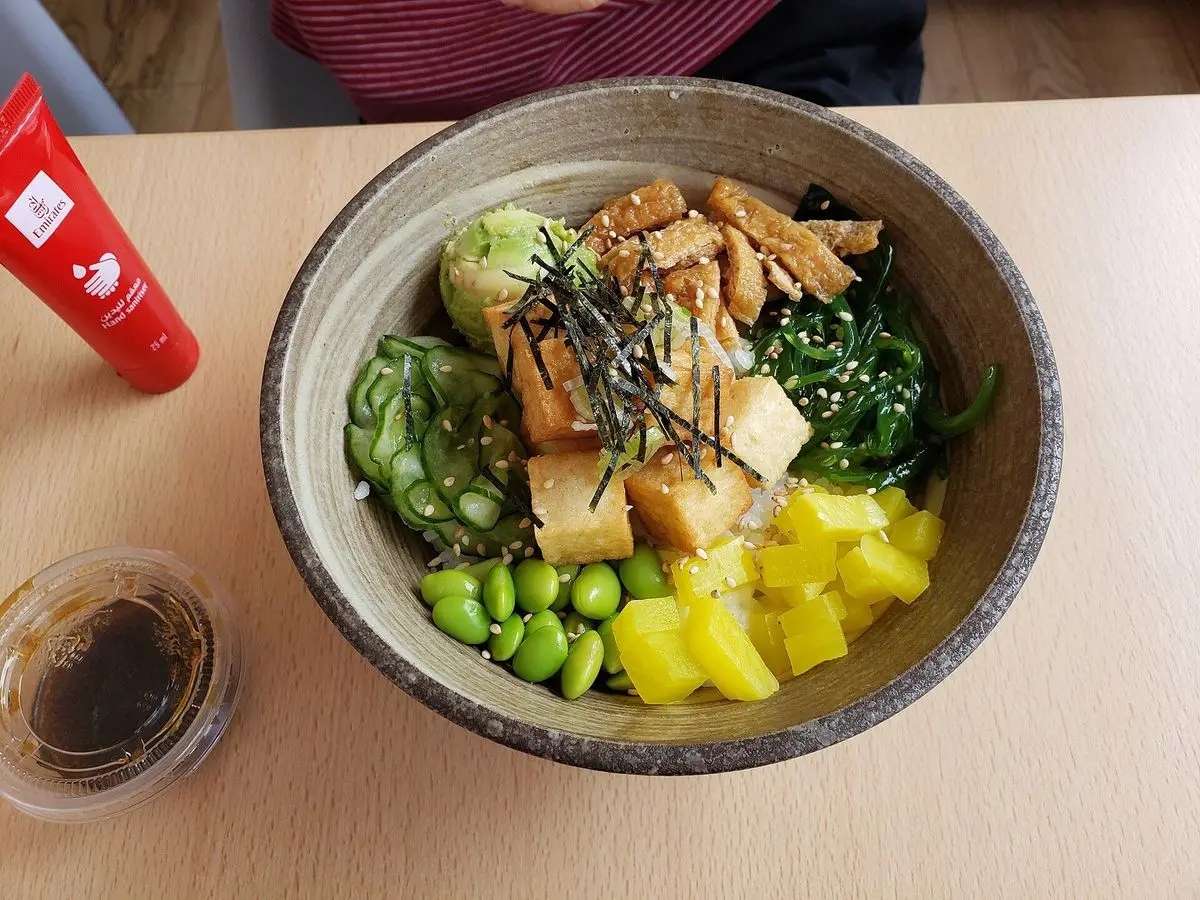 Cuenco de poke con tofu en tiras, edamame, mango en dados, algas y arroz, visto desde arriba