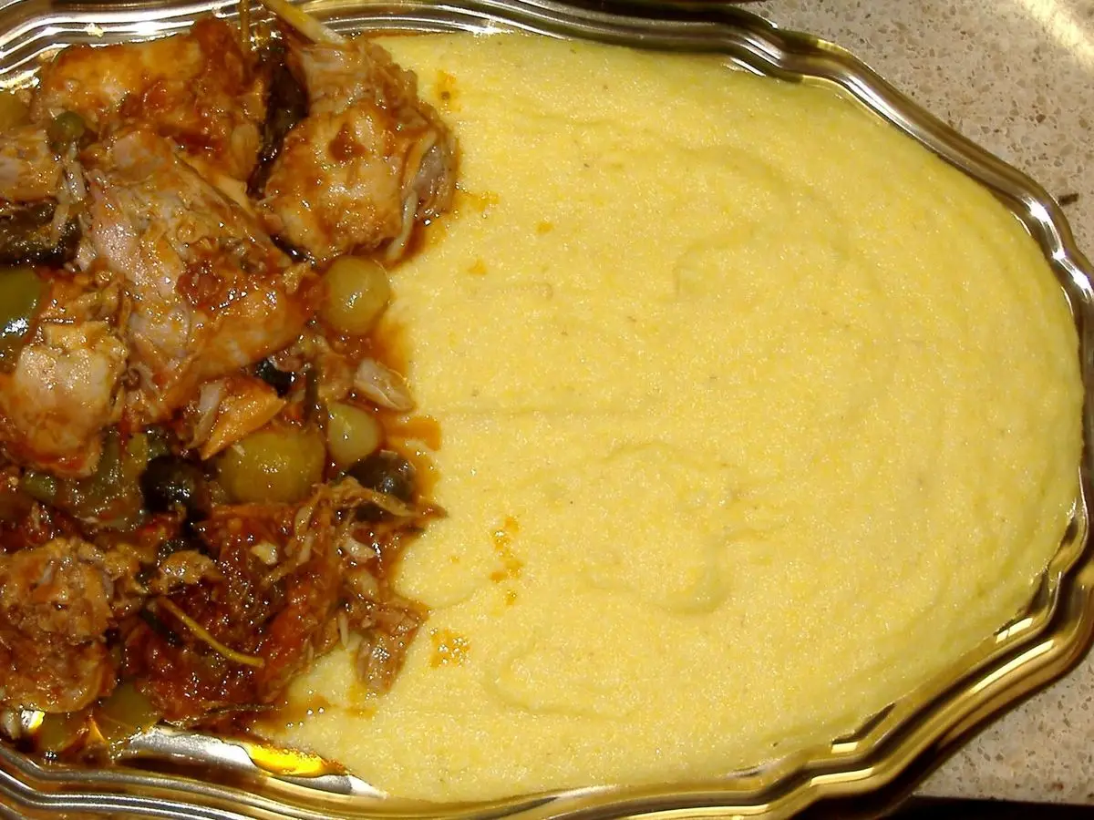 Conejo guisado con aceitunas y salsa de tomate junto a polenta cremosa amarilla en una fuente