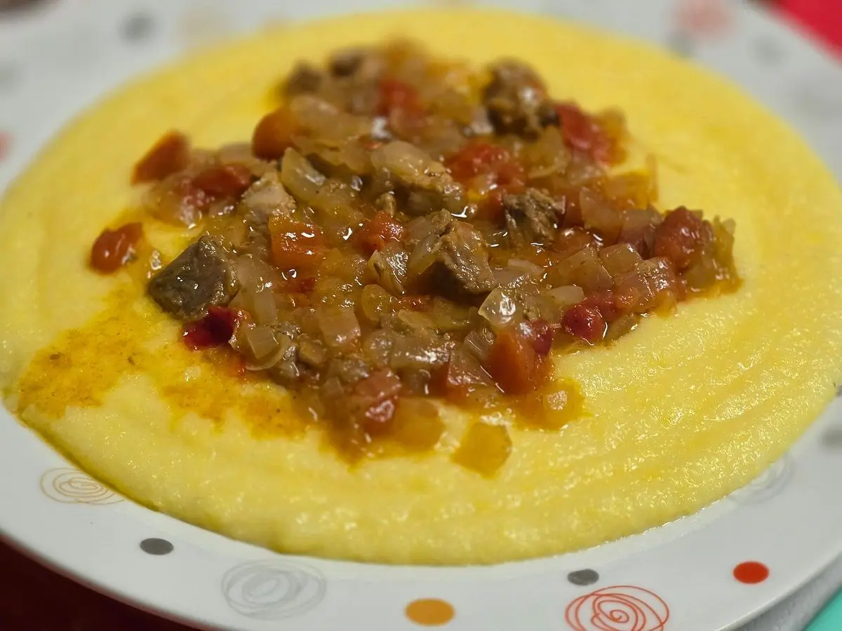 Plato blanco de polenta amarilla cremosa cubierta con un guiso de verduras y tomate