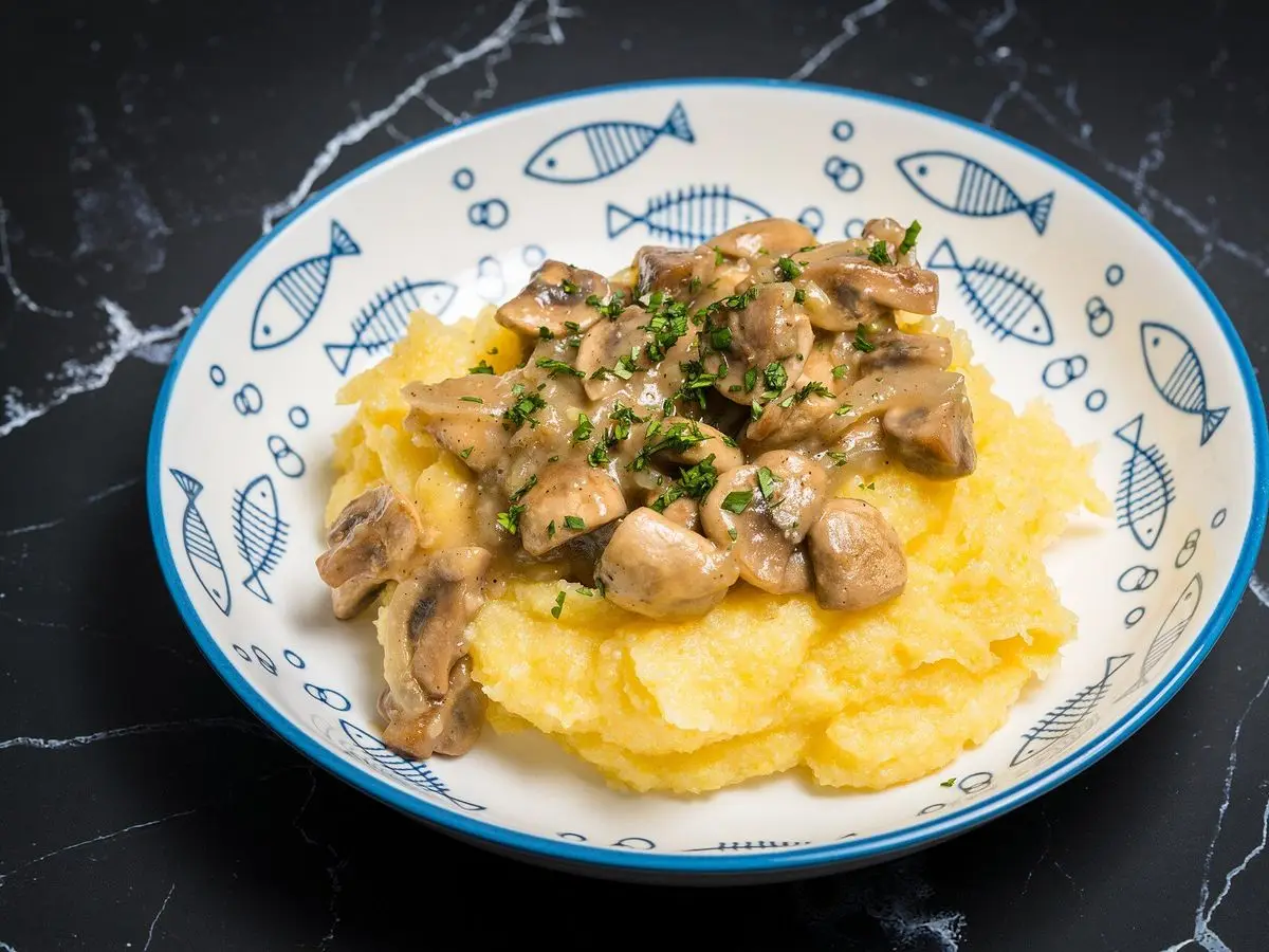 Polenta cremosa con salteado de champiñones y perejil en un cuenco blanco decorado con peces azules